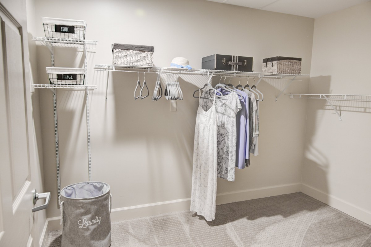 A well-organized closet with clothes hanging on a rod and storage boxes on shelves.