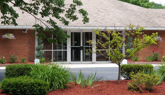 A well-landscaped house with a porch and large windows, surrounded by lush plants and trees.