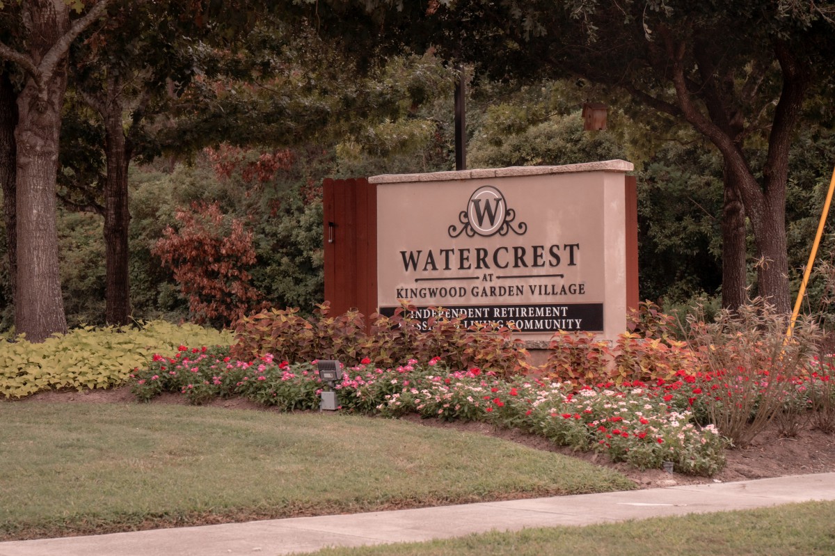 A landscaped entrance sign for Watercrest at a residential village surrounded by flowers and trees.
