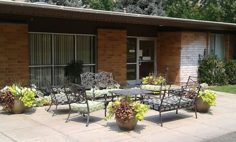 A cozy patio area with metal furniture and potted plants outside a brick building.