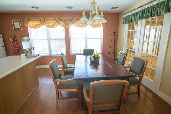 A cozy dining room with a large table, surrounded by chairs, and illuminated by natural light from the windows.
