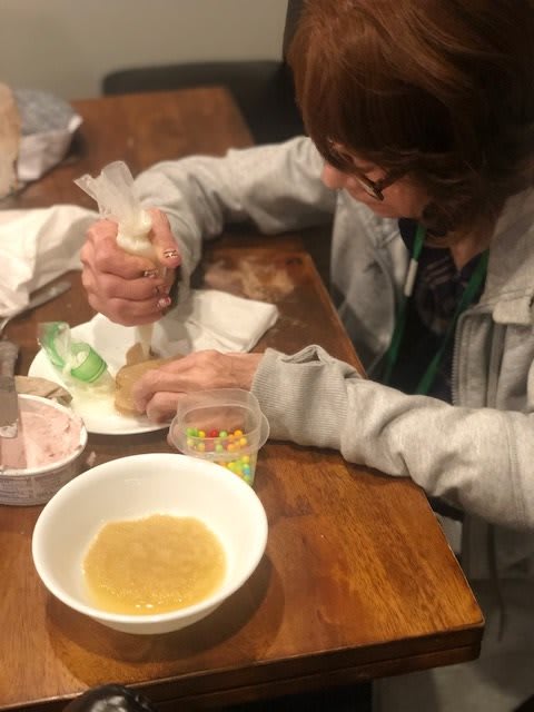 A person decorating a cupcake with icing at a table.