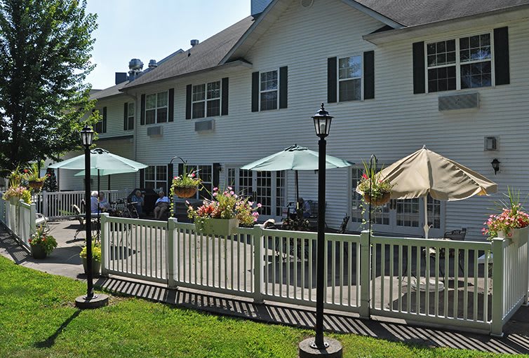 A sunny day at a patio with umbrellas and outdoor seating in front of a two-story building.