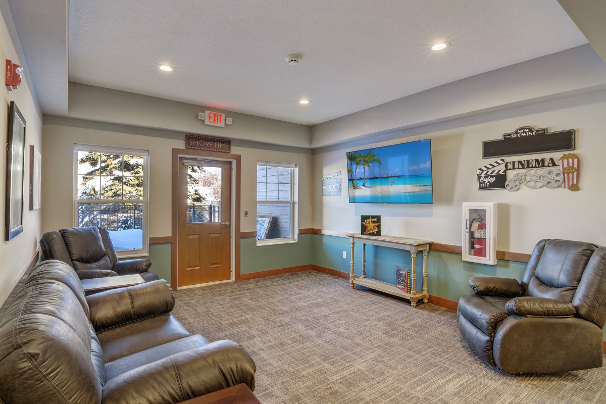 A cozy waiting room featuring leather chairs, a large television, and decorative posters on the walls.