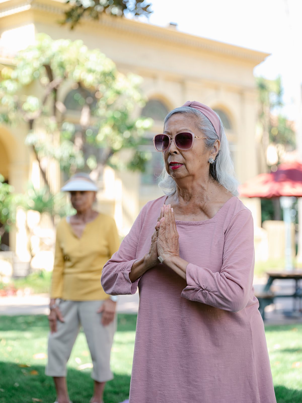 An elderly woman practicing yoga and meditation outdoors in a park setting.