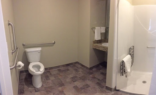 A view of a simple bathroom with a toilet, sink, and accessible features.