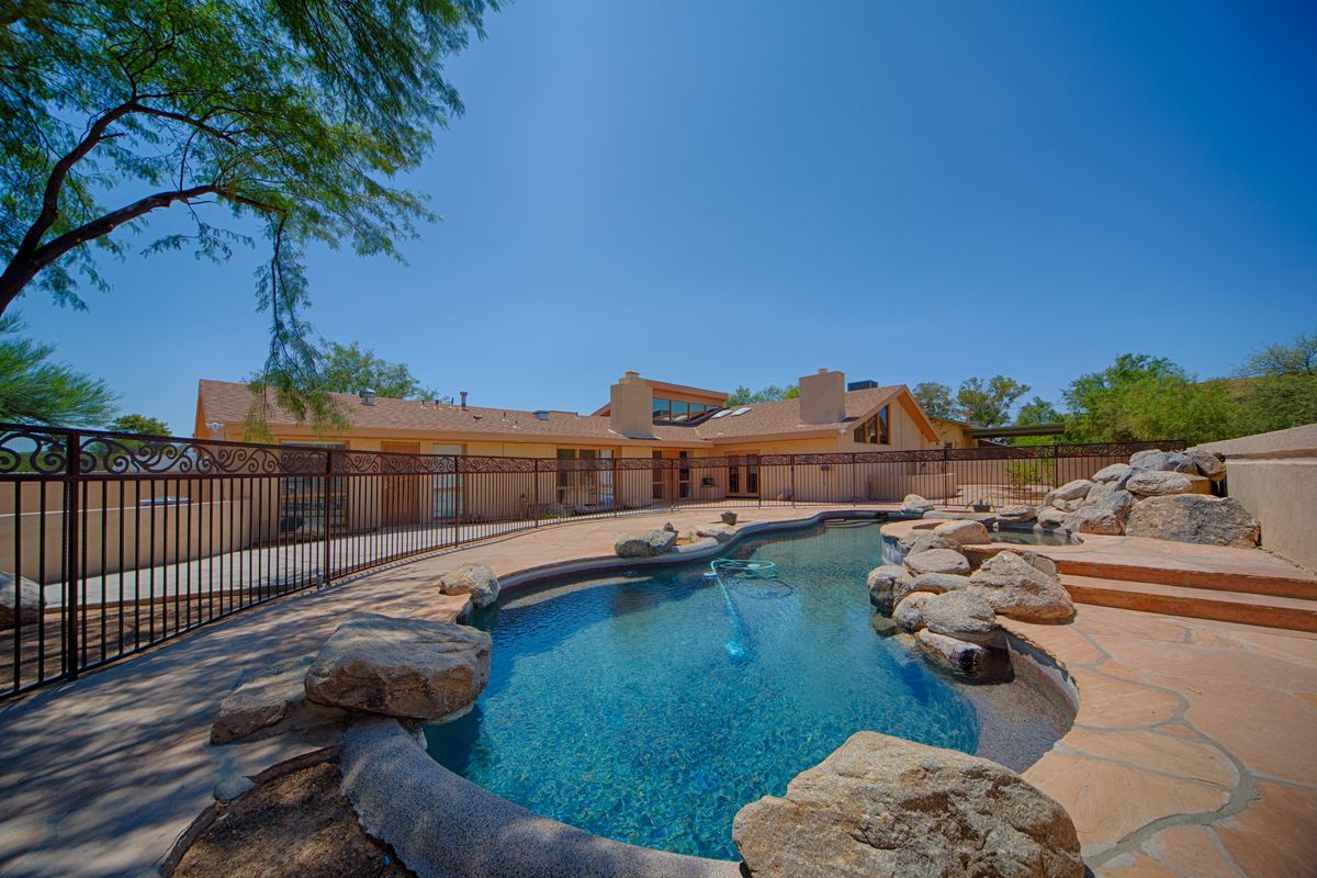 A serene backyard with a swimming pool surrounded by rocks and trees on a sunny day.
