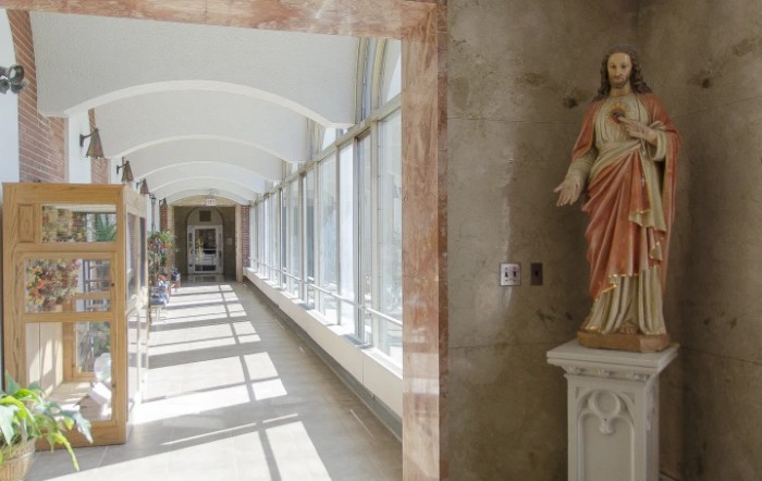 A sunlit corridor featuring a statue alongside large windows.