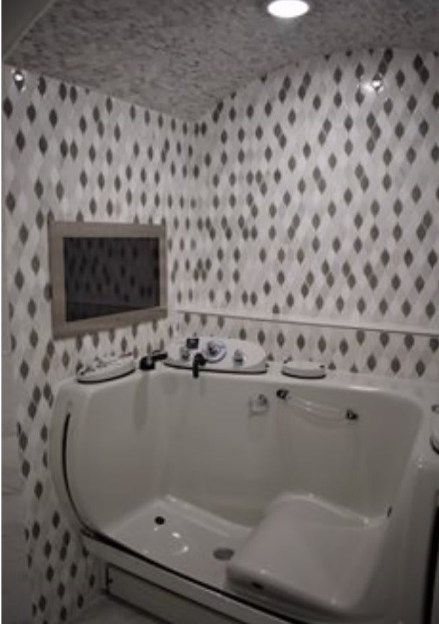 A bathroom with a corner bathtub and patterned tile walls.