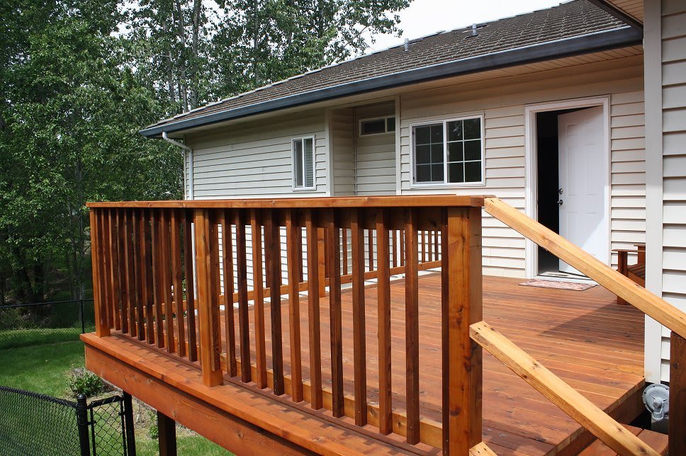 A wooden deck with a railing attached to the exterior of a house.