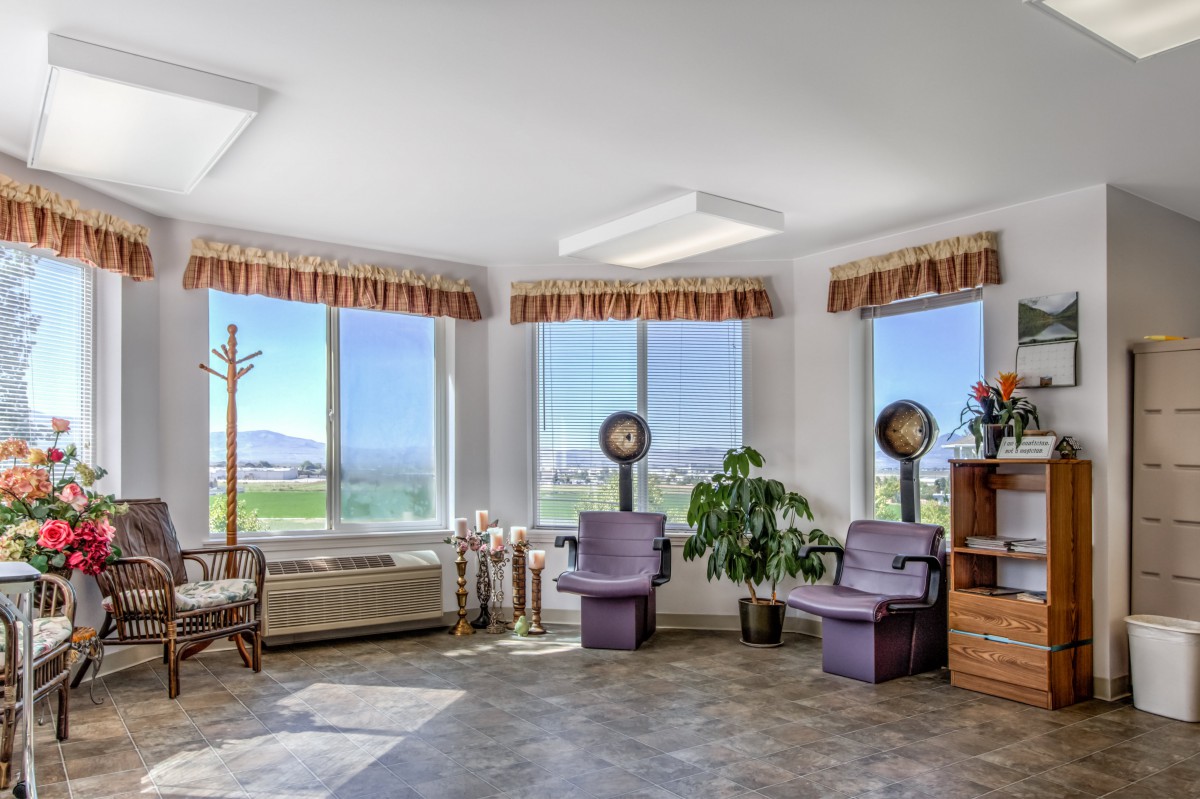 A bright salon waiting room with hairdryer chairs and large windows overlooking a scenic view.