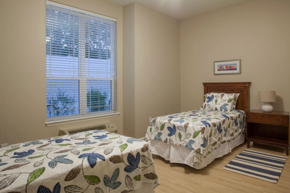 A cozy bedroom with two twin beds featuring decorative bedding and a large window letting in natural light.