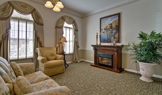 A cozy living room with classical decor, featuring a fireplace, armchair, and elegant curtains.