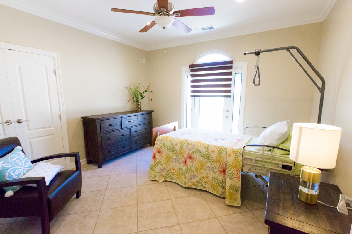 A well-lit bedroom with a hospital bed, dresser, and ceiling fan.