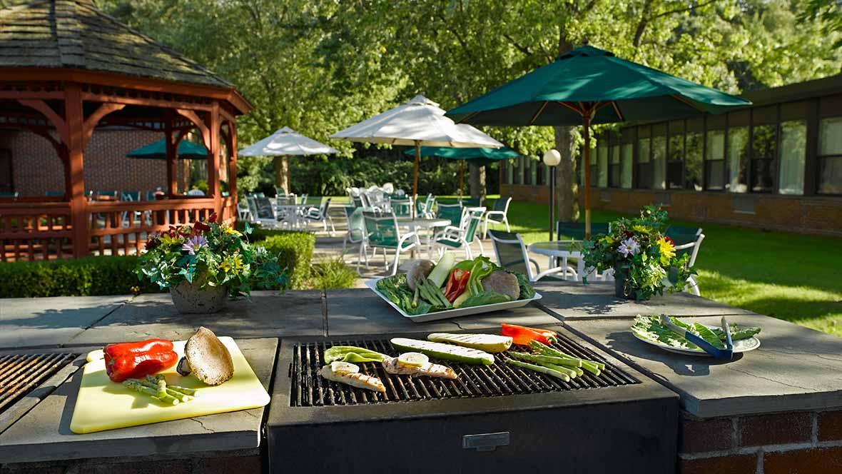 An outdoor barbecue setup with vegetables grilling on a sunny day in a garden patio.