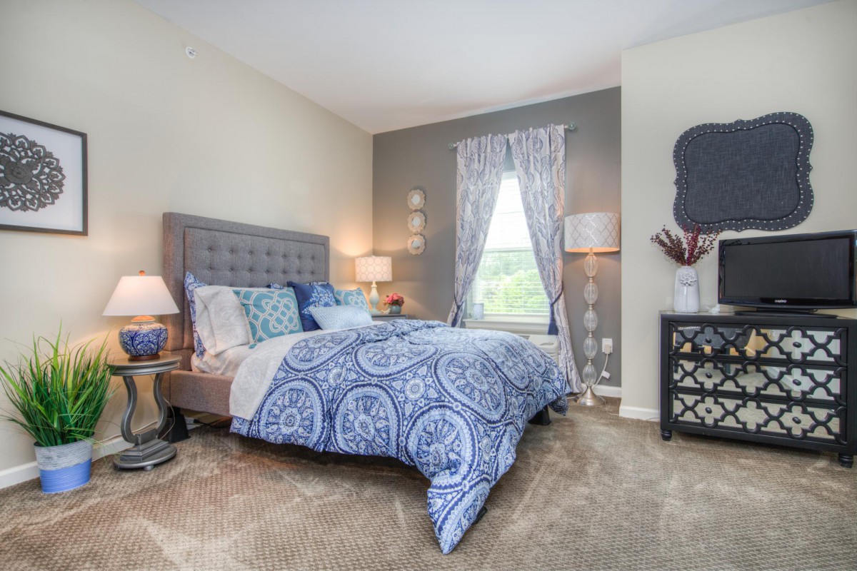 A cozy bedroom with elegant decor, featuring a bed with blue patterned bedding, matching curtains, and soft lighting from table lamps.
