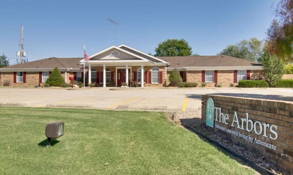 A single-story brick building with a white entrance and green lawn, featuring a sign in the foreground.