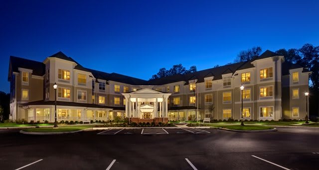 A well-lit hotel building at night with a spacious parking lot.