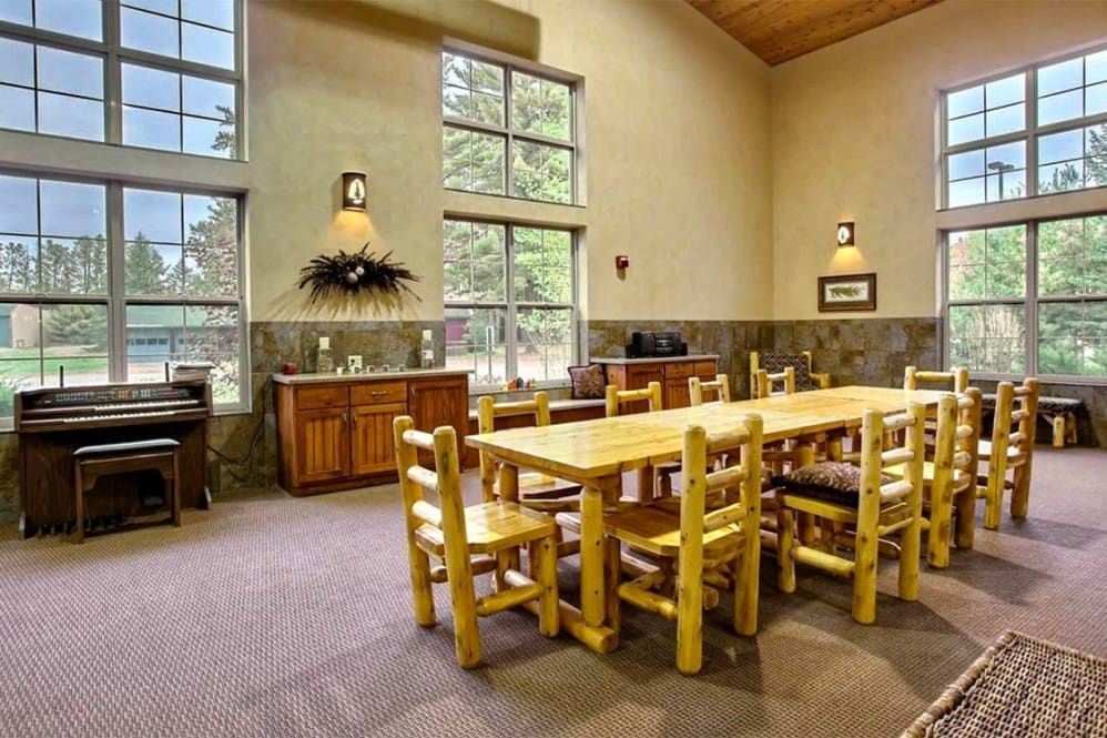 A rustic dining room with wooden furniture and large windows.