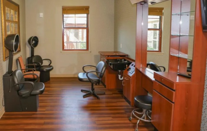 An empty hair salon with chairs and mirrors, featuring wooden flooring and windows.