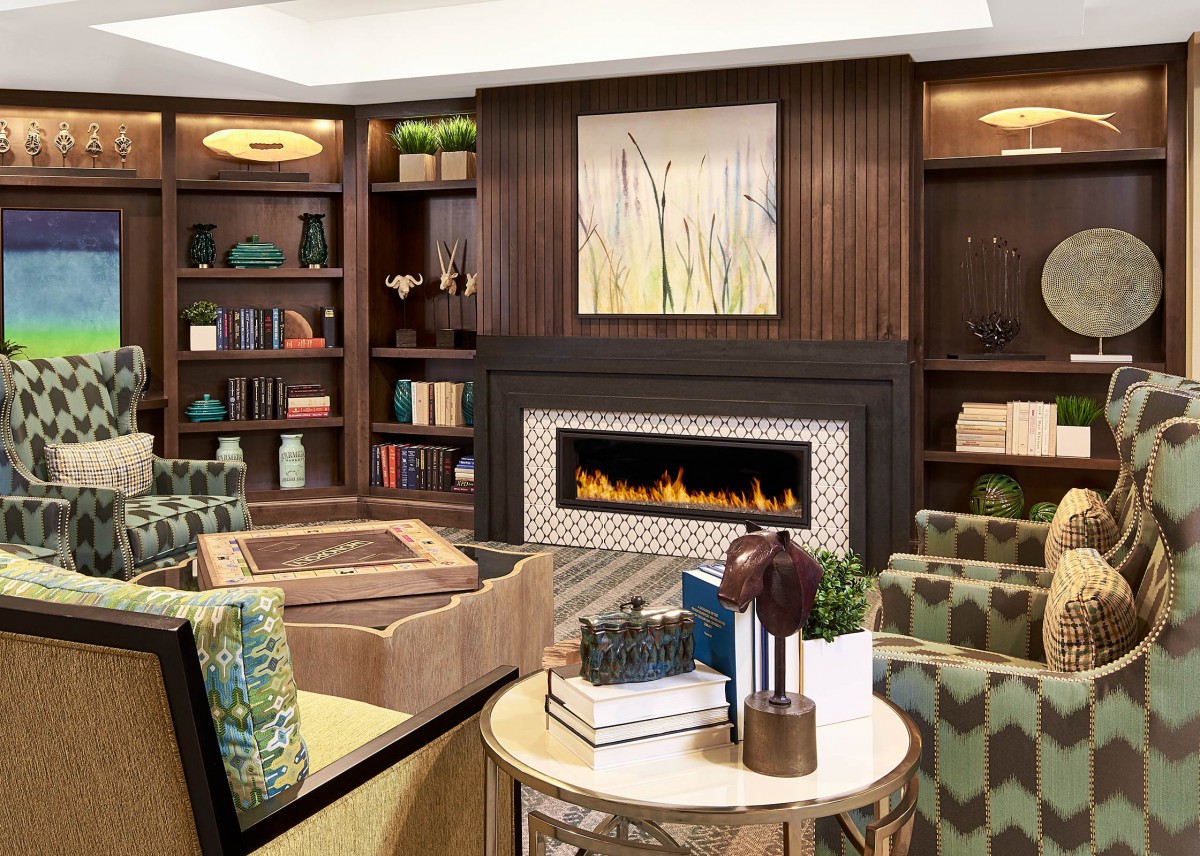 A cozy living room features a modern fireplace, surrounded by elegant bookshelves and comfortable seating.