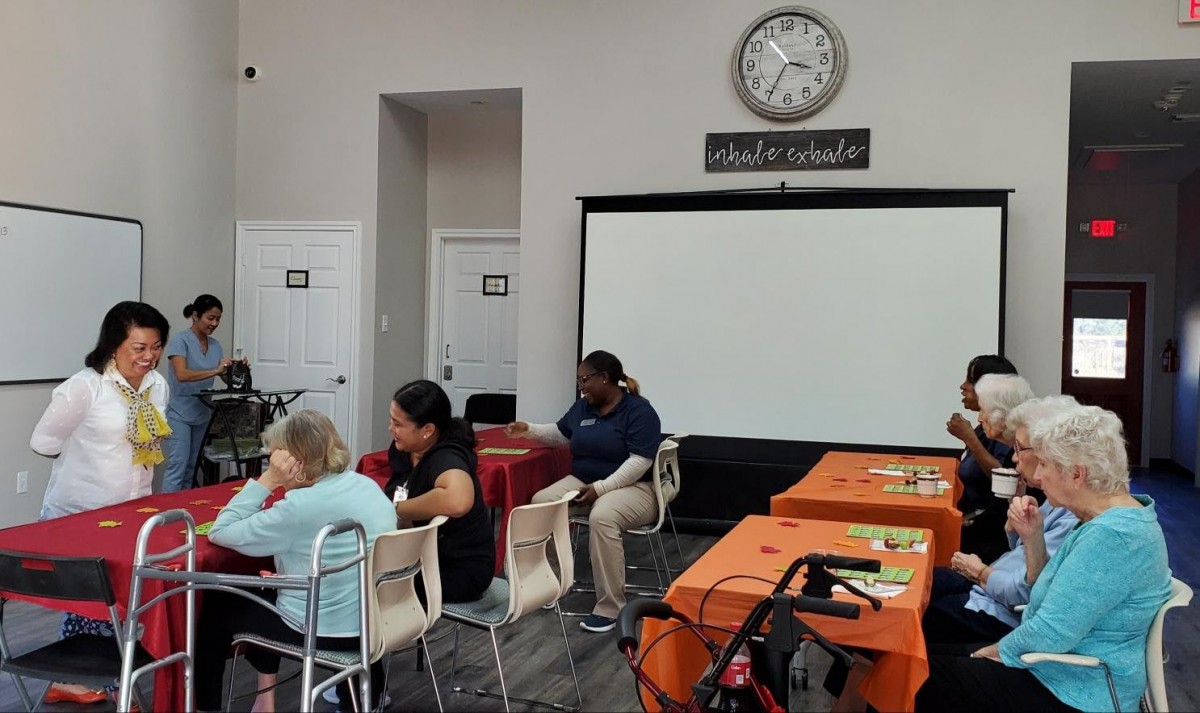 A community center gathering with people sitting around tables covered in orange tablecloths.