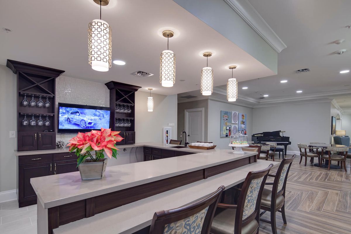 A modern bar area featuring sleek pendant lights, a spacious countertop with chairs, and a decorative flower arrangement.