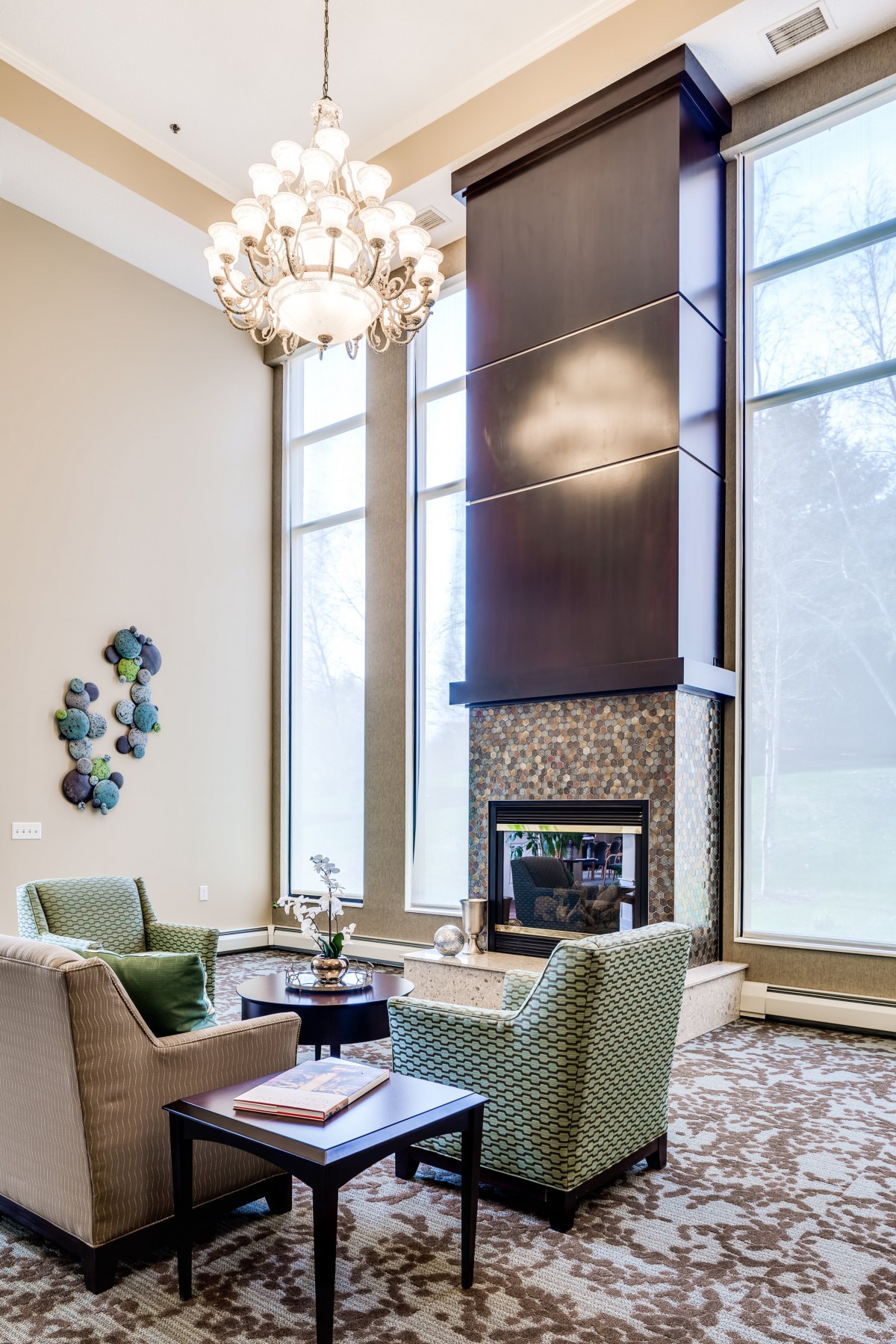 A modern living room featuring a high ceiling, large windows, and a central fireplace with comfortable seating.