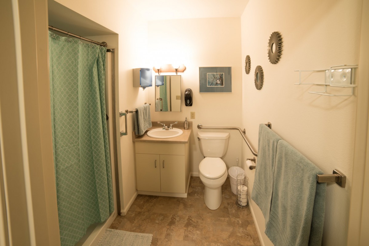 A neatly organized bathroom with a sink, toilet, and shower curtain, accented with light green towels and wall decor.