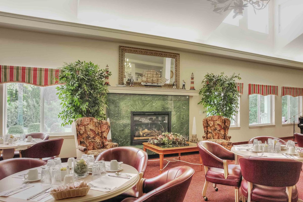 A cozy dining area featuring a fireplace, surrounded by elegant chairs and tables with decorative plants.