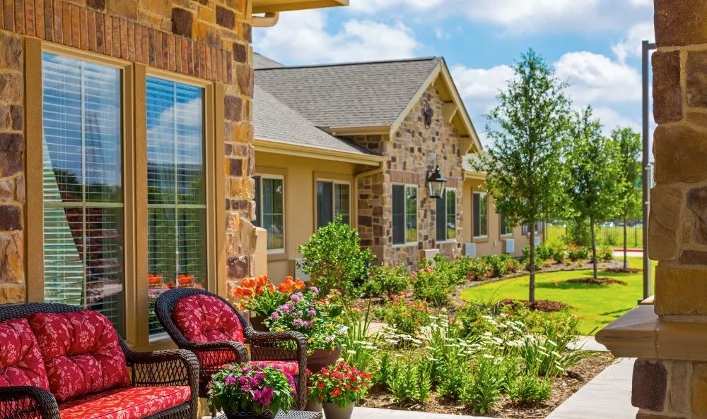 A beautiful garden with colorful flowers and patio furniture in front of a house with a brick exterior.