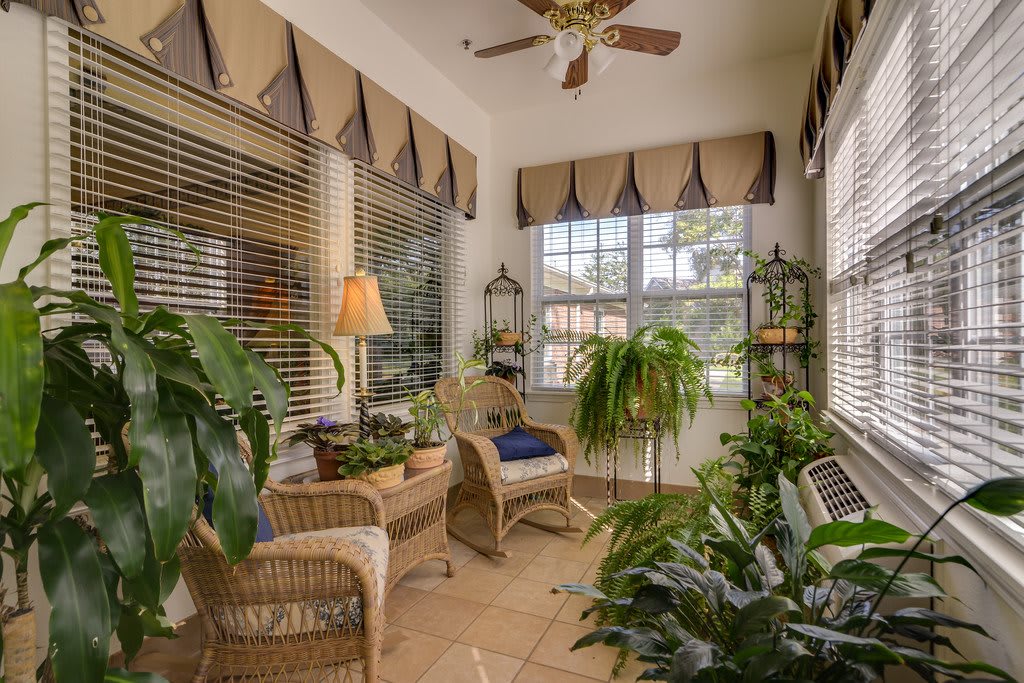 A cozy sunroom filled with natural light, featuring wicker furniture and lush indoor plants.