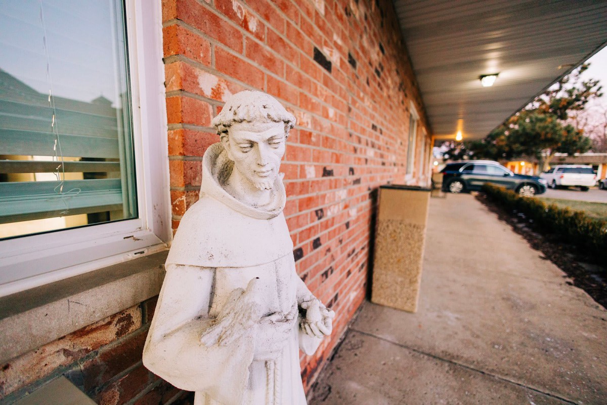 A statue stands by a brick wall outside a building.