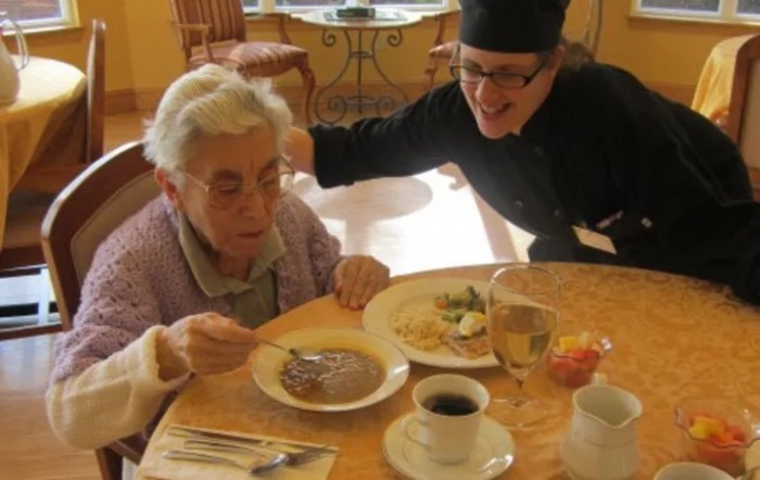 An elderly person enjoys a meal with assistance from a caregiver.