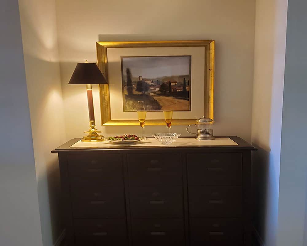A neatly arranged interior setup featuring a chest of drawers, a stylish lamp, and framed artwork.