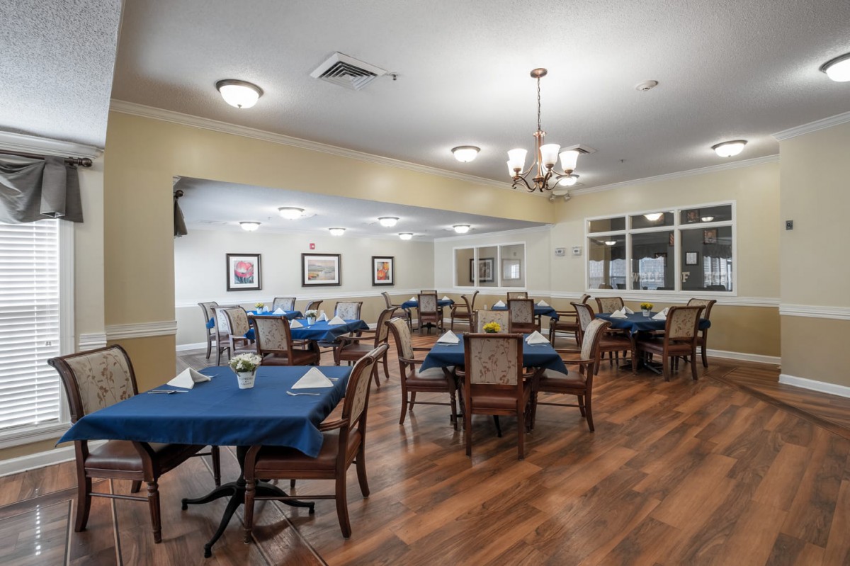 A well-arranged dining area with multiple tables and chairs, featuring a wooden floor and elegant lighting.