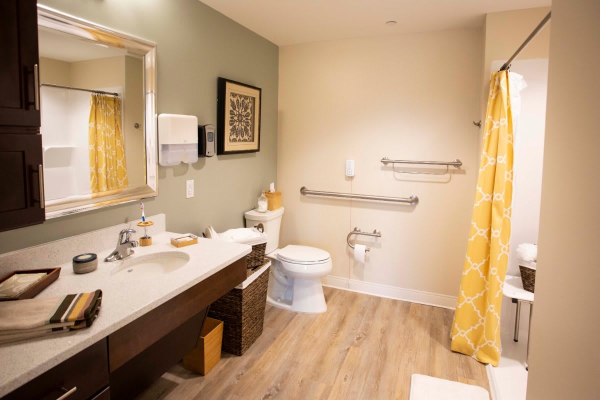 A modern bathroom with wooden flooring, featuring a sink, toilet, and yellow shower curtain.