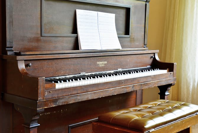 An upright piano with sheet music resting on its stand and a bench in front.