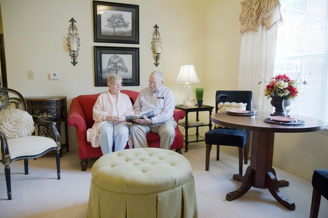 An elderly couple sitting on a red sofa in a cozy living room, engaged in reading.