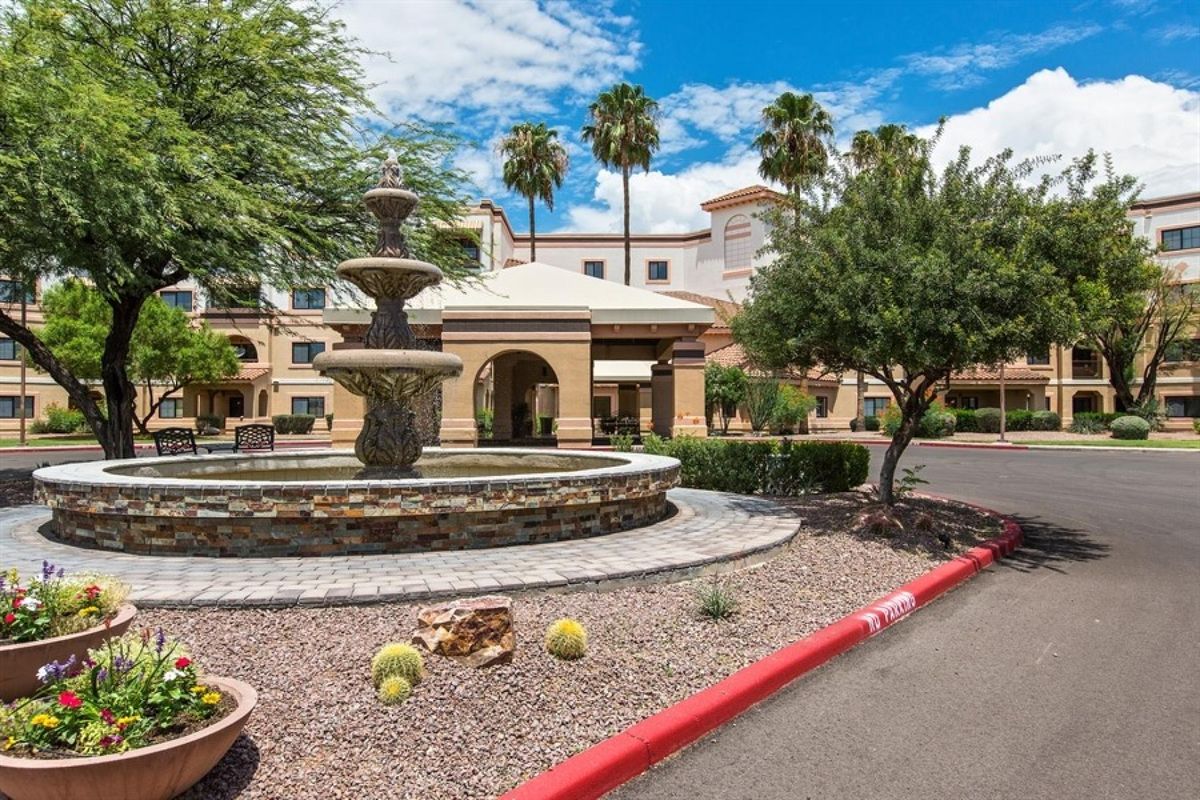 A sunny day at a building entrance with a fountain and desert landscaping.