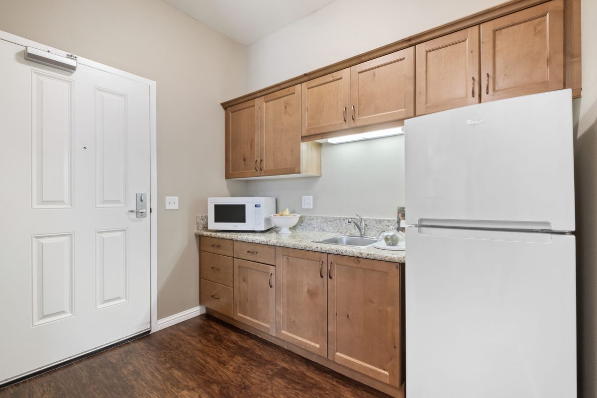A compact kitchen with wooden cabinets, a microwave, a refrigerator, and a sink.