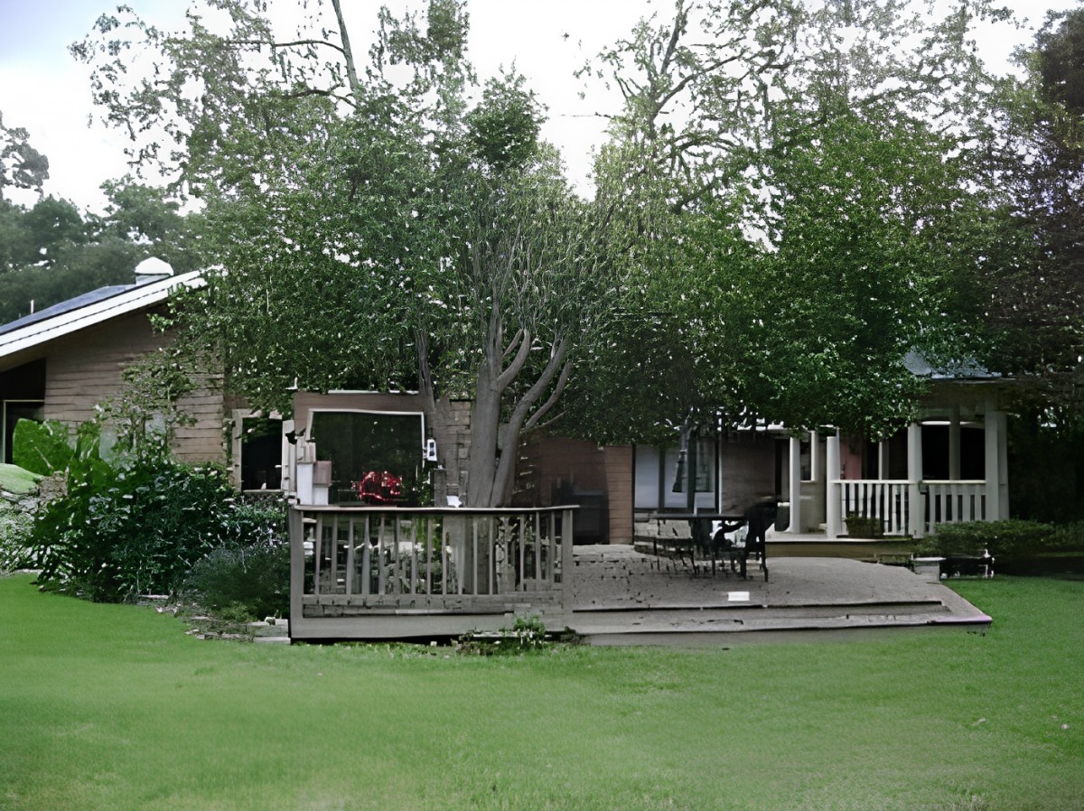 A cozy house with a wooden deck surrounded by lush trees and a green yard.