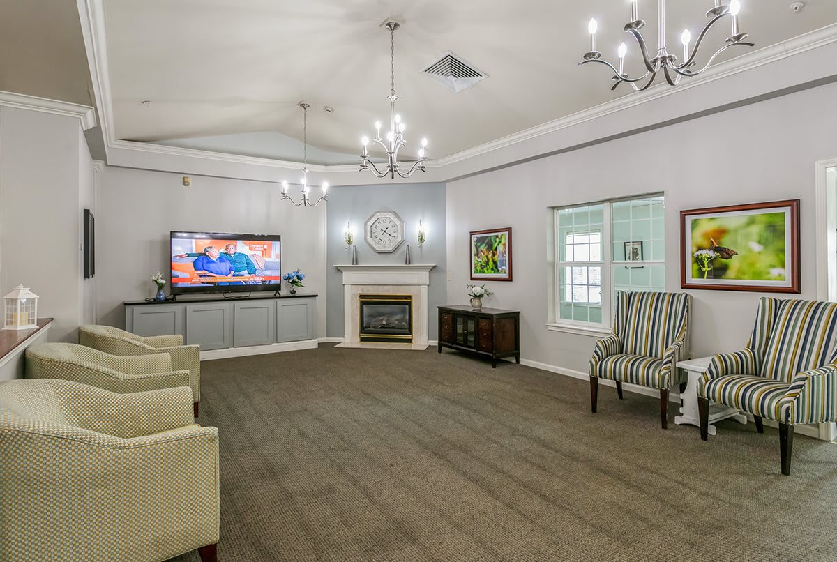 A spacious living room featuring a fireplace, television, and elegant chandeliers with comfortable seating and artwork on the walls.