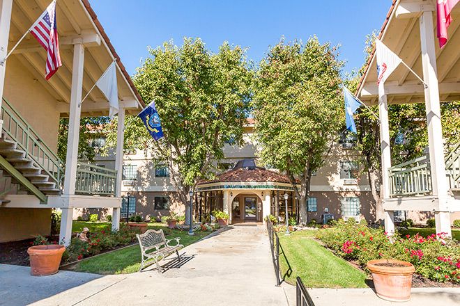 A scenic view of a building entrance surrounded by trees and a well-maintained garden on a sunny day.