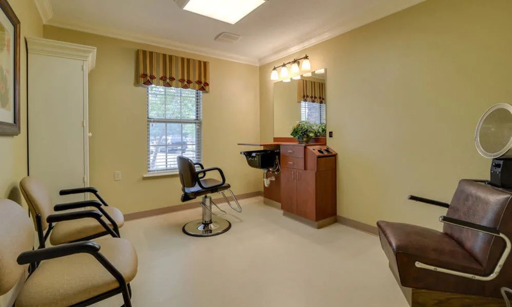 An empty hair salon room with a chair, mirror, and window.