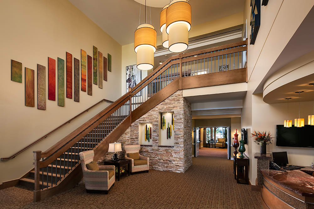 A modern lobby interior featuring a staircase with wooden railings, comfortable seating arrangements, and elegant lighting fixtures.
