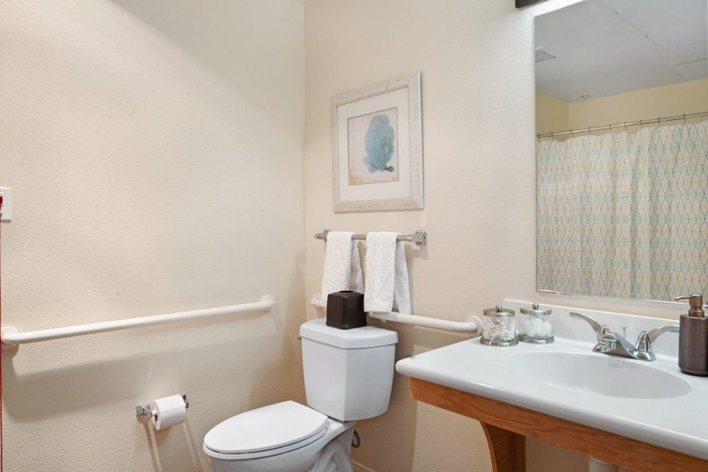 A clean bathroom with a toilet, sink, and mirror, featuring white walls and neatly arranged towels.