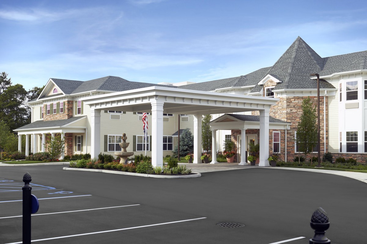 A view of a building entrance with an overhang, surrounded by a parking lot and landscaped areas.
