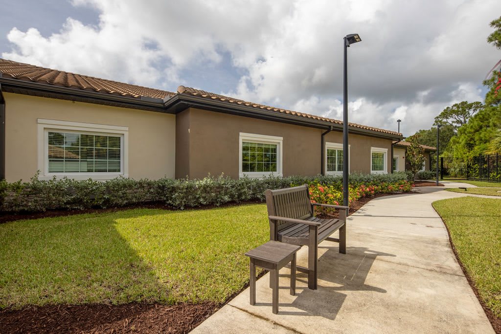 A serene outdoor space with a bench and landscaped garden in front of a building under a cloudy sky.
