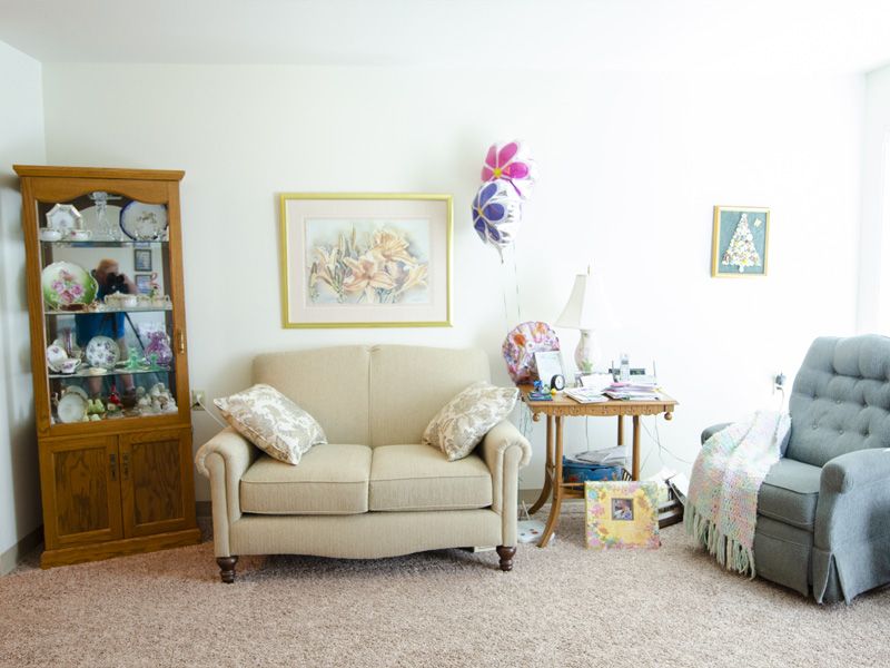 A cozy living room with a beige sofa, decorative pillows, and a corner cabinet showcasing various items.